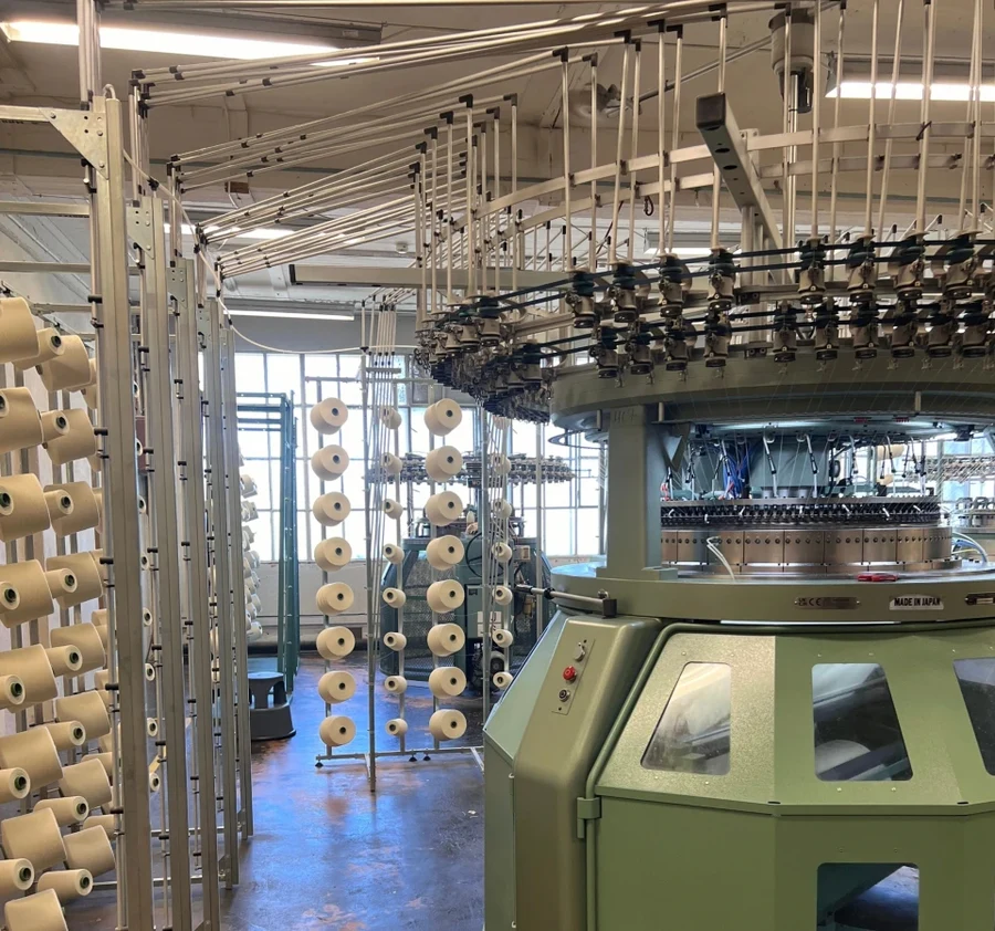 Circular knitting equipment with yarn cones feeding the needle bed on a factory floor